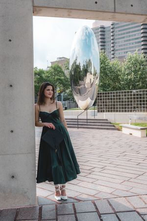 Woman in green dress posing beside large reflective silver sculpture in urban plaza.