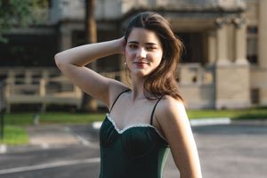 Young woman in green dress poses with hand in hair on sunny urban street.