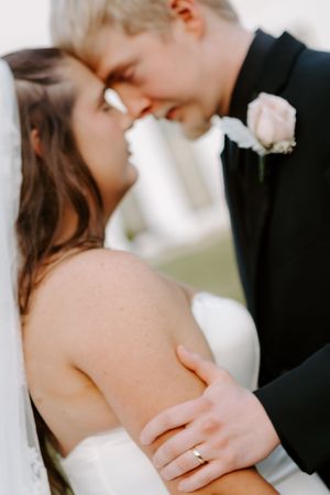 Close-up of bride and groom sharing romantic moment with wedding ring visible on her hand.