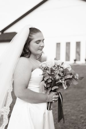 Black and white portrait of a bride in a strapless gown holding a bouquet with eyes closed outdoors.