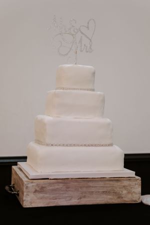 Four-tier square white wedding cake with Mr and Mrs topper on a rustic wooden stand.