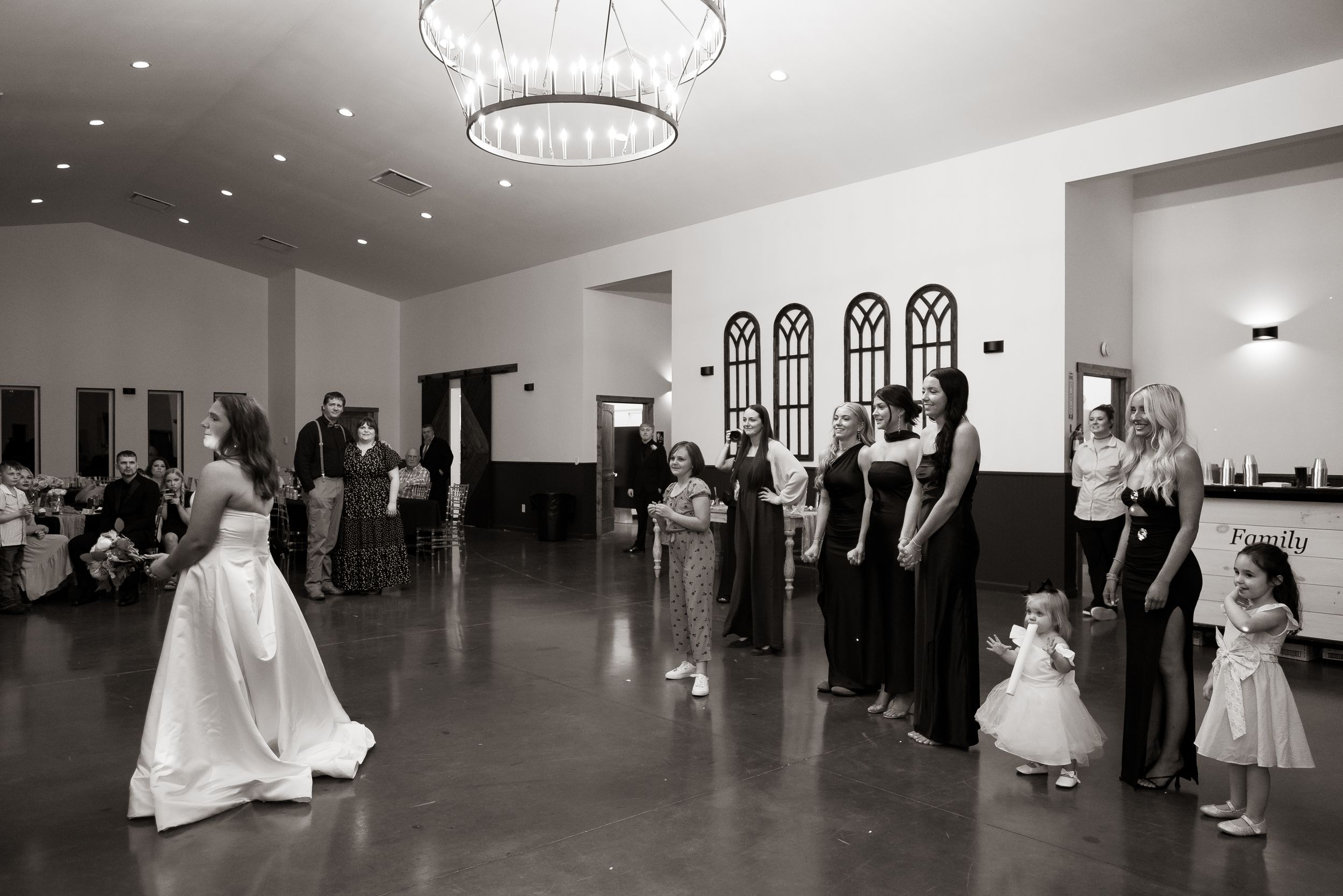 Bride prepares to toss bouquet to bridesmaids and guests in elegant black and white wedding reception.