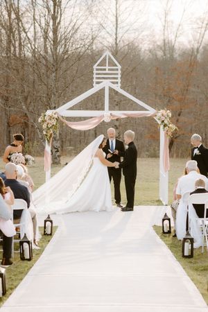 Bride and groom exchange vows at outdoor wedding altar adorned with pink flowers and draping.