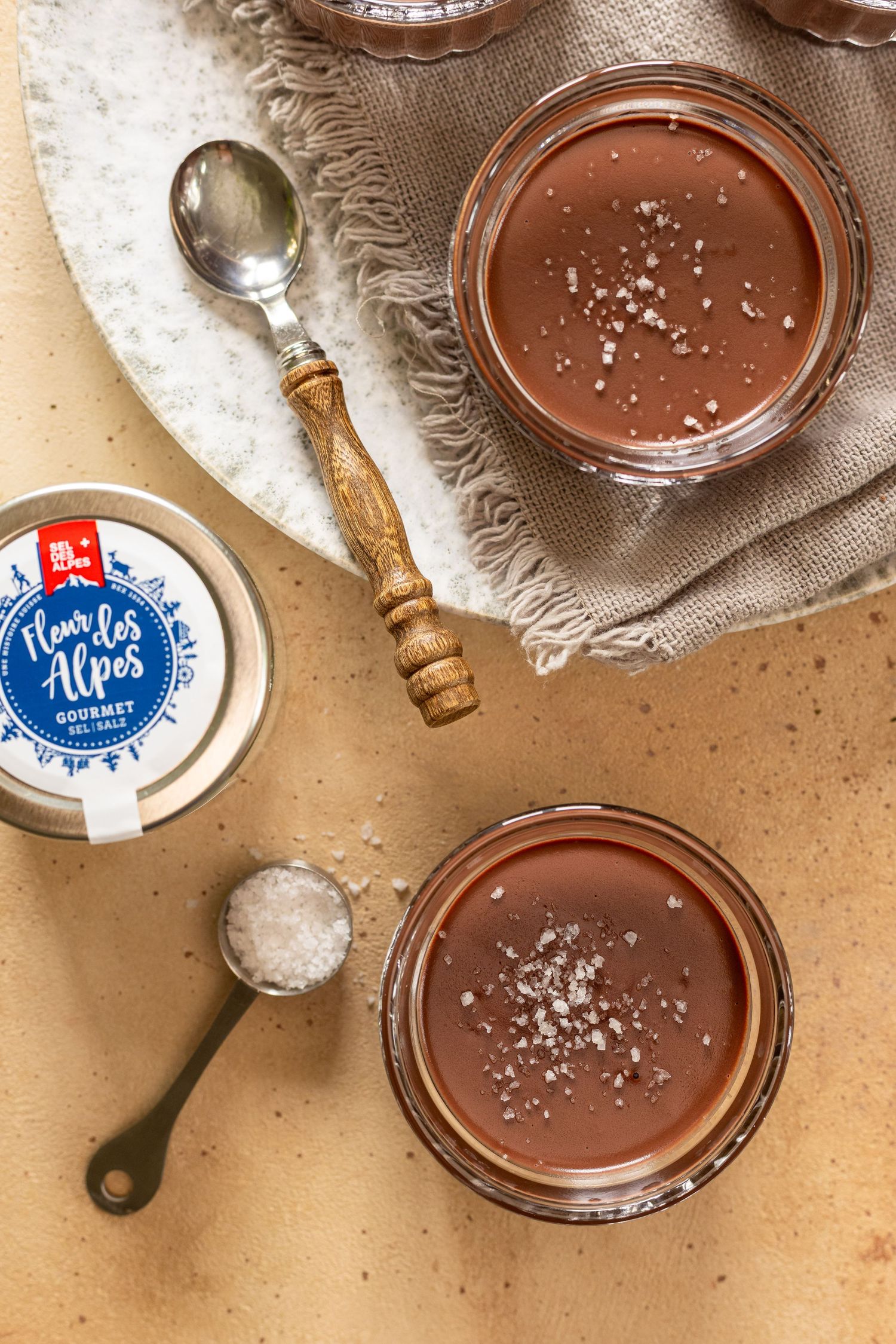 Chocolate mousse desserts in glass jars with dark chocolate chunks scattered on a light surface.