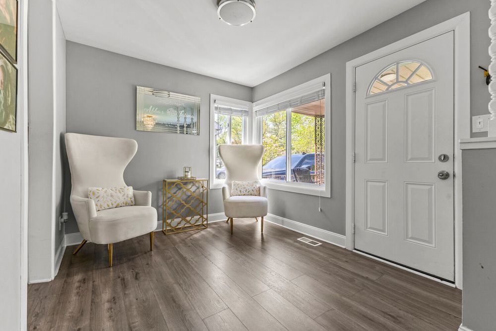 Entryway with dark hardwood floors, two accent chairs, white front door with transom window.