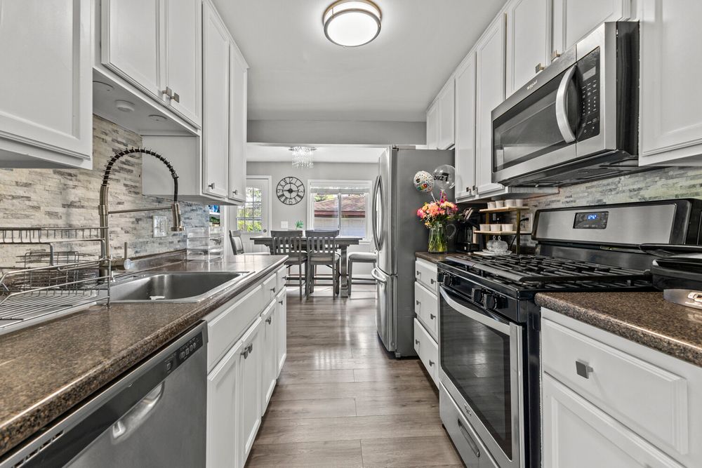 Modern galley kitchen with white cabinets, dark granite countertops, stainless steel appliances, and hardwood floors.