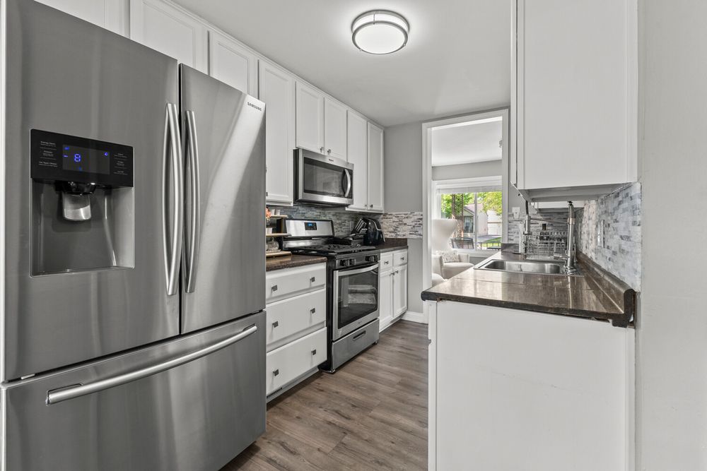 Bright white kitchen featuring stainless steel French door refrigerator, gas range, and marble tile backsplash.