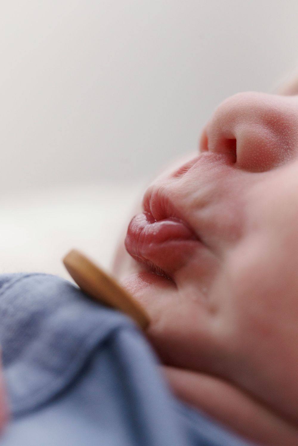 Close-up of a sleeping newborn baby's face with full lips and tiny nose, wearing a blue outfit.