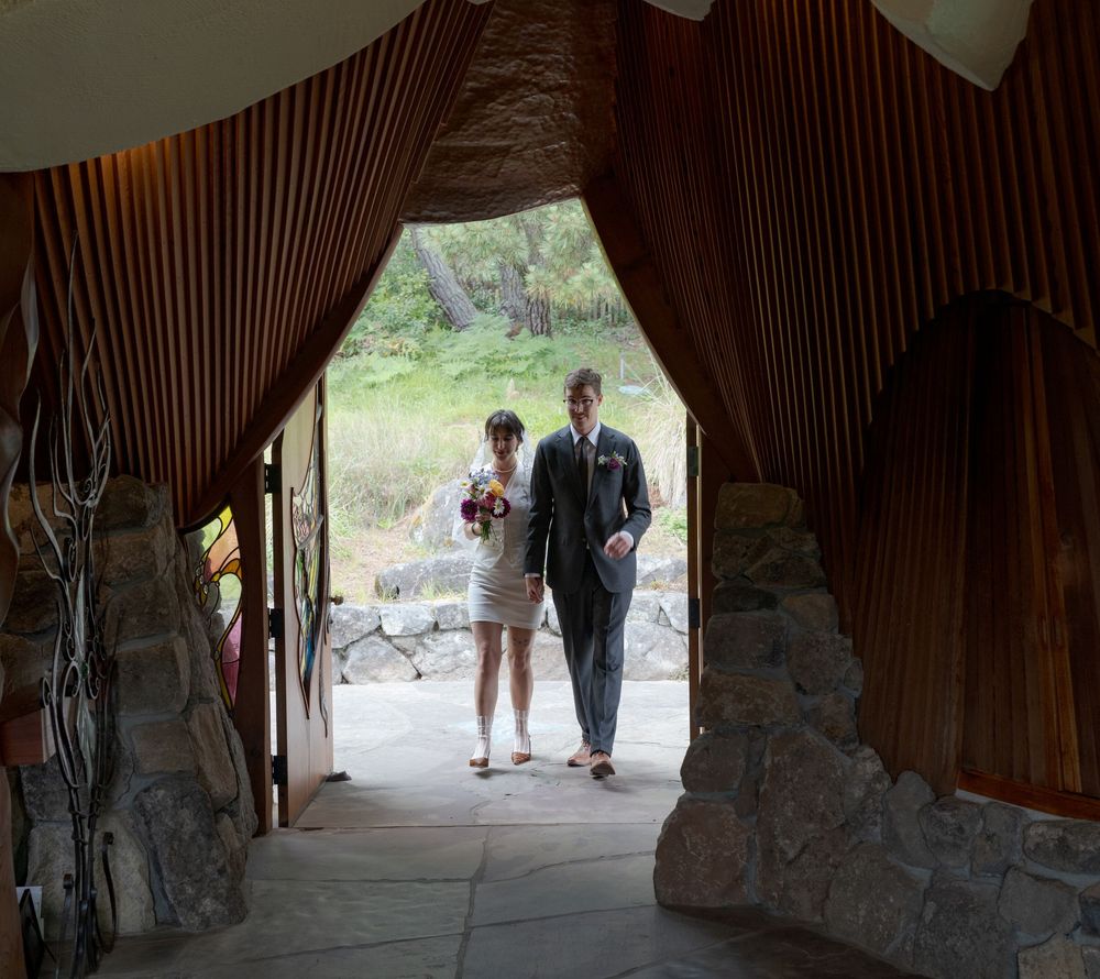 Bride and groom enter wedding venue through elegant wood-paneled archway with stone walls.