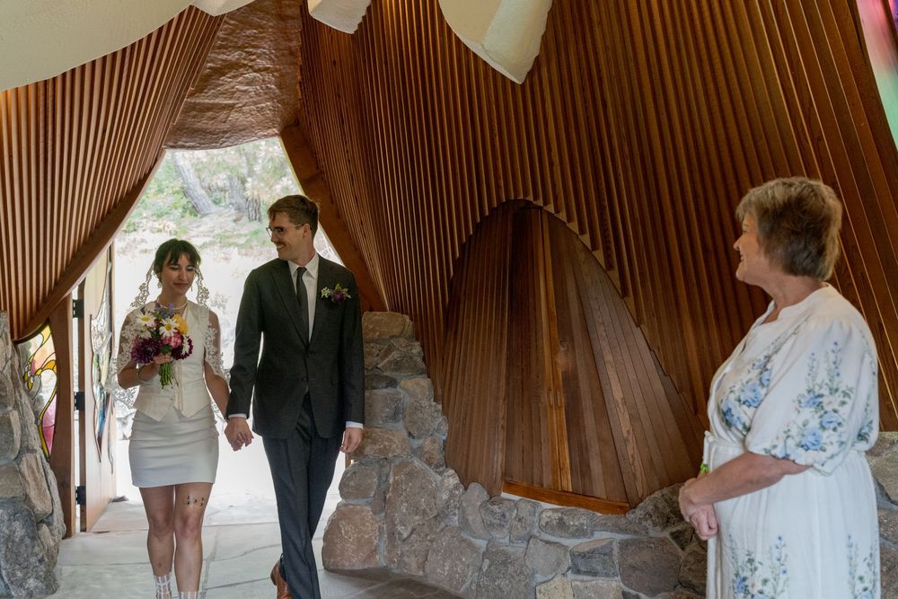 Couple holding hands in a stunning wooden chapel with curved timber walls, greeted by an officiant on their wedding day.