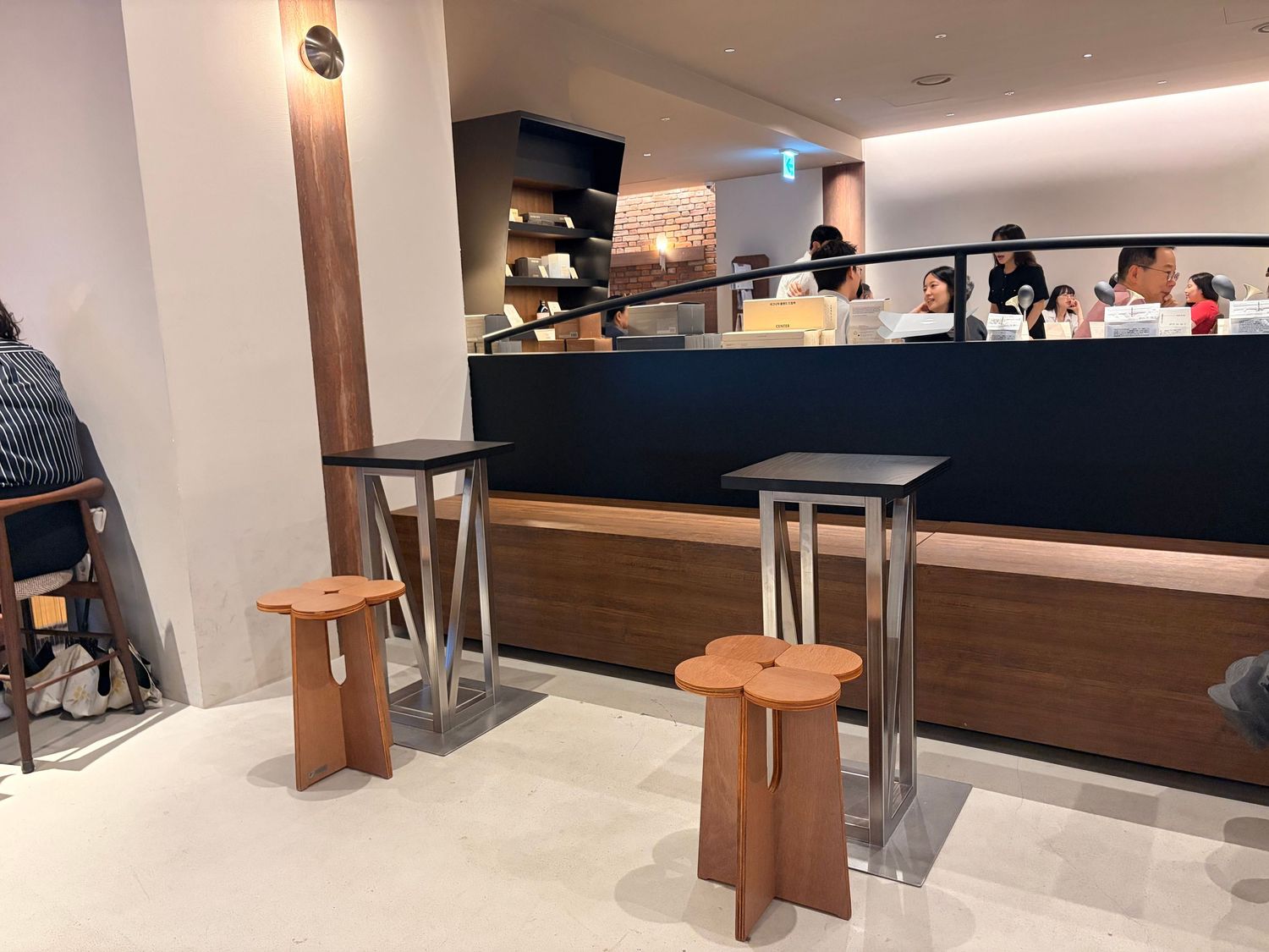 Modern cafe interior with high tables, wooden stools, and customers at a sleek dark counter.