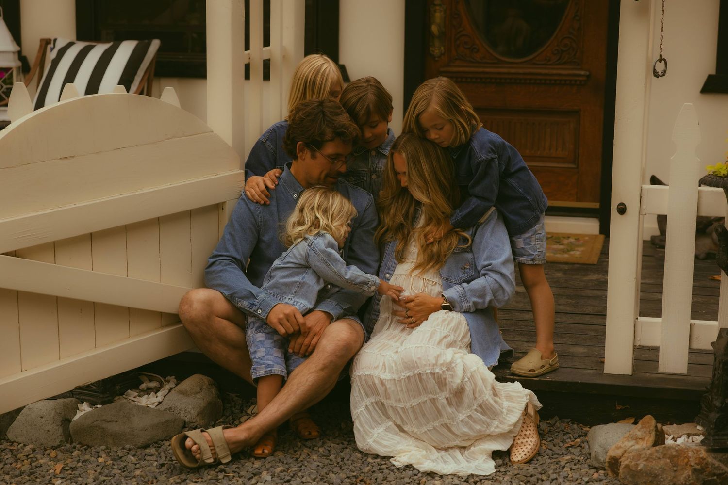 Family of five in denim outfits sharing a tender moment on porch steps, captured by an Orange County family photographer.