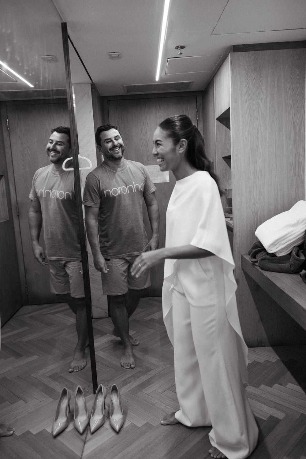 Bride and groom smiling together in dressing room mirror reflection.