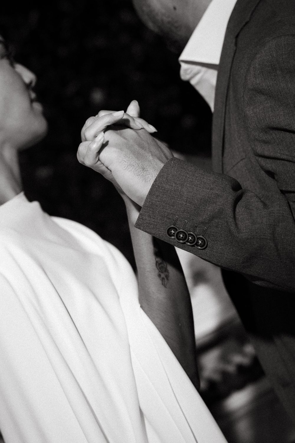 Groom holding bride's hands tenderly during wedding ceremony in black and white.