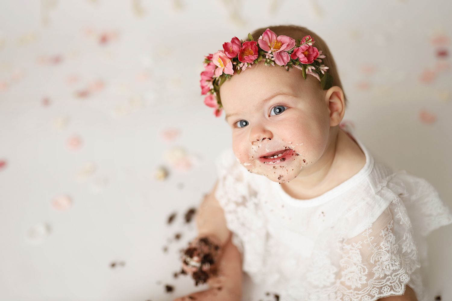 Adorable baby girl with chocolate cake on her face wearing white lace dress and pink floral crown. Utah County cake smash photographer
