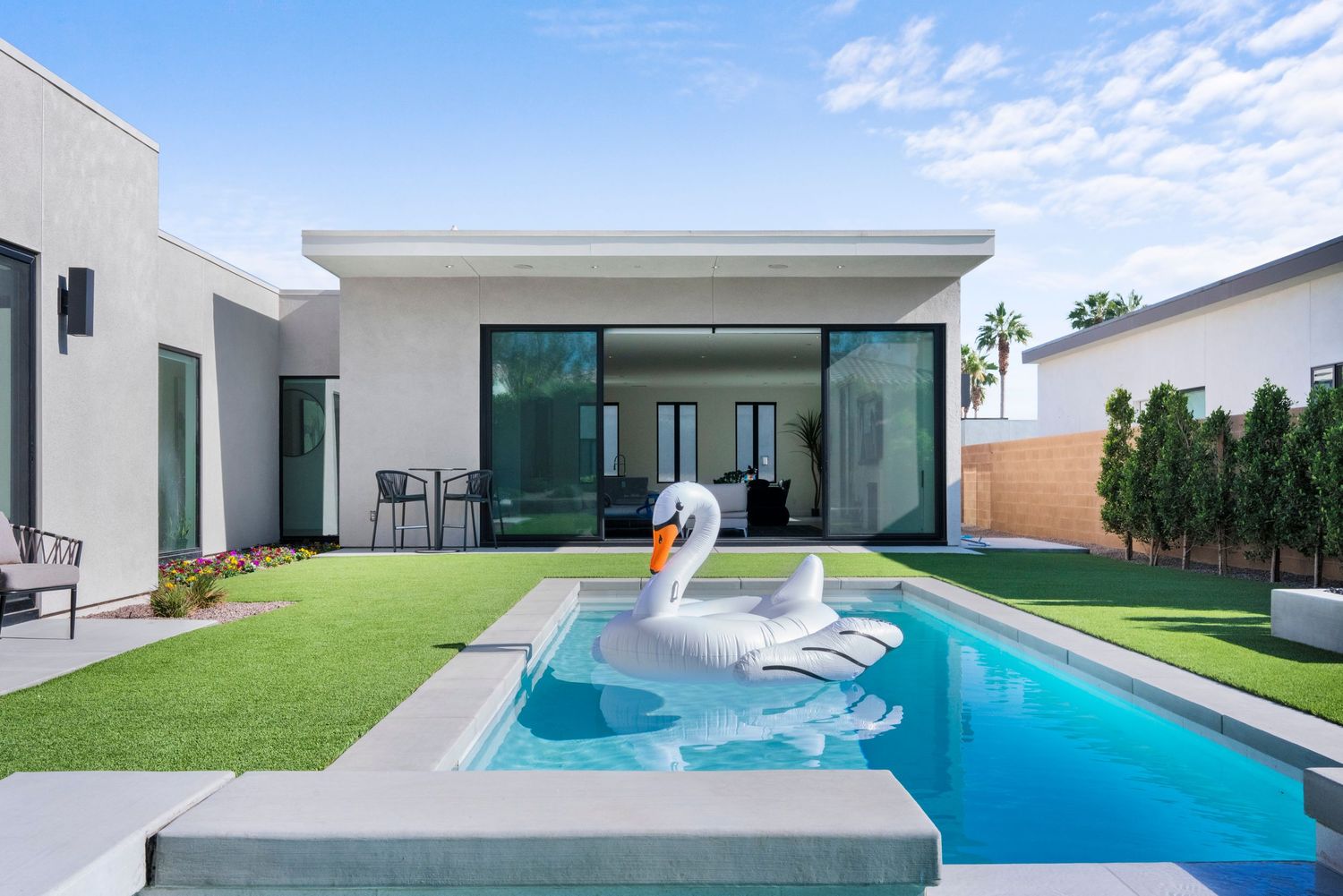 Modern home with a sparkling pool featuring a swan float, lush green lawn, and sleek indoor-outdoor living space.