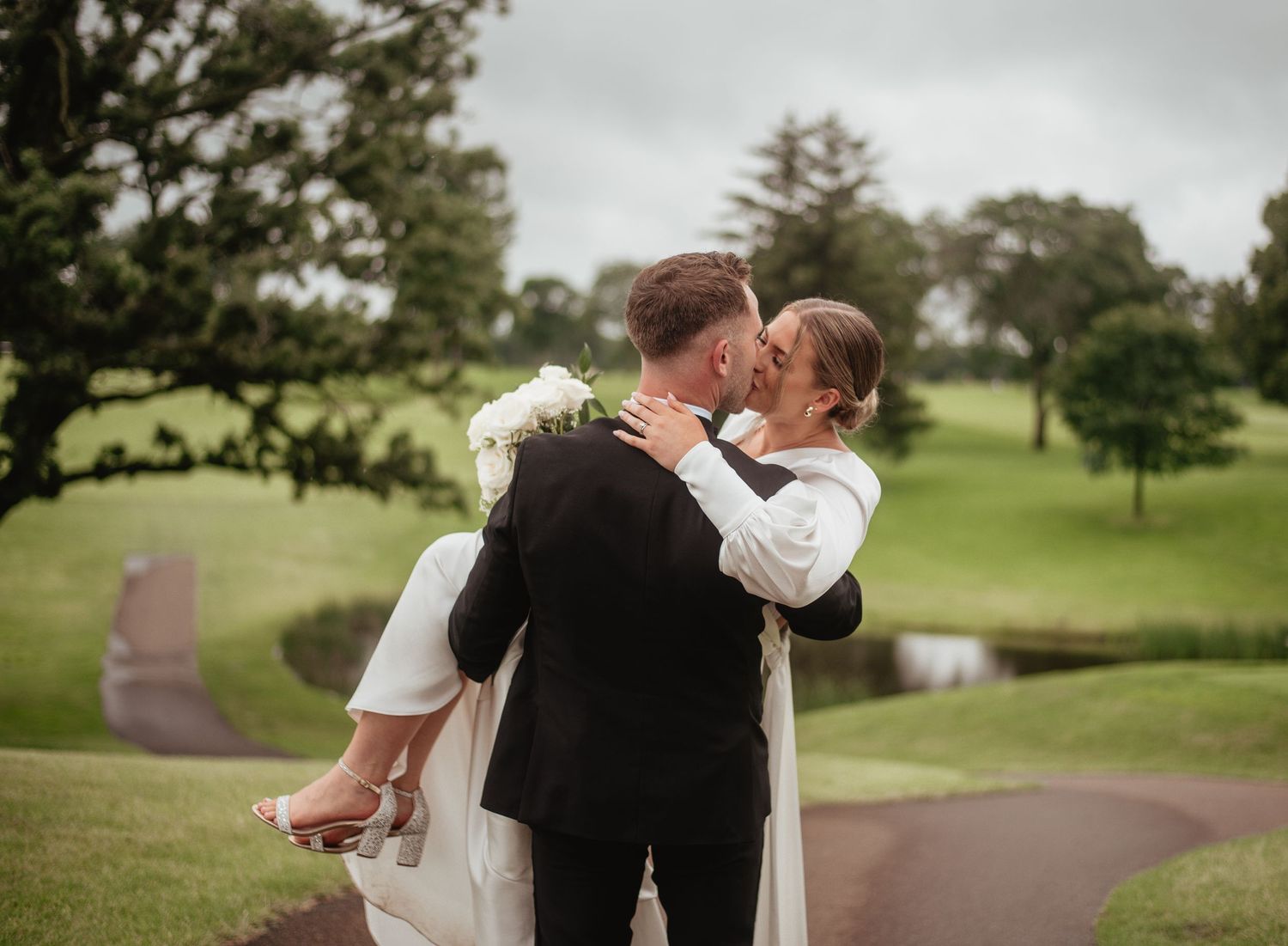 A romantic wedding portrait on a grassy hill with soft, dreamy lighting.