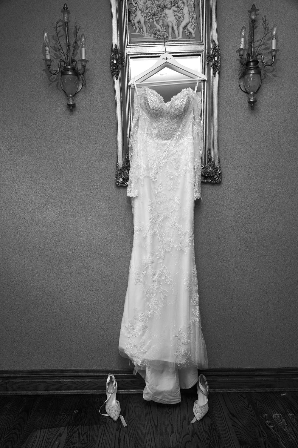 White lace wedding dress displayed on wall with ornate sconces and framed artwork.