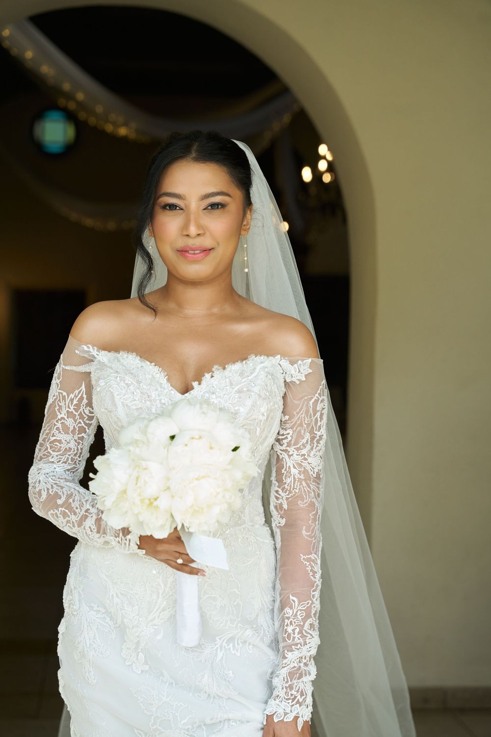 Bride in traditional white lace wedding dress holding white flower bouquet.