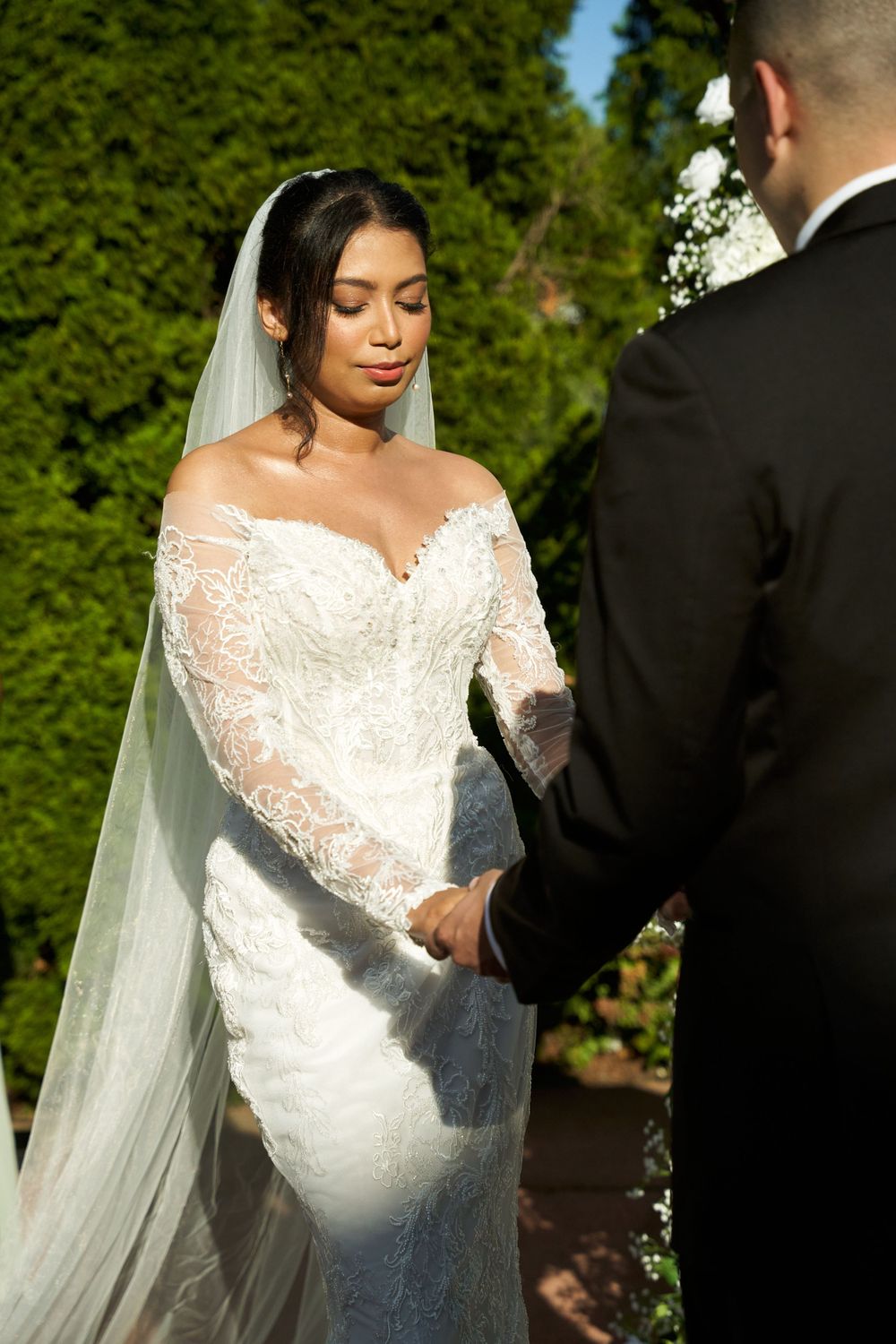 Sunlit wedding ceremony showcasing intricate lace details of bridal gown and veil.