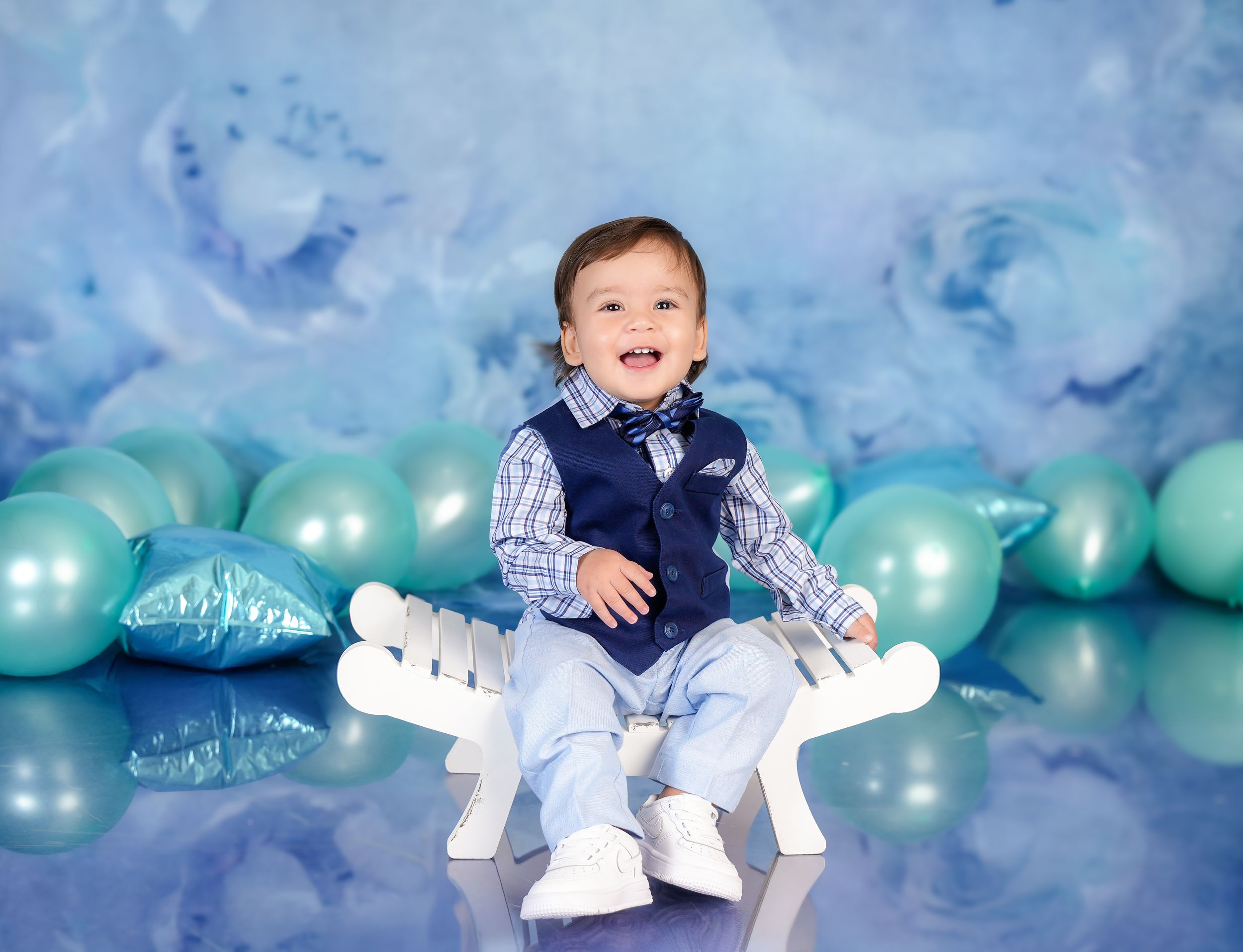 Little one sitting on white dinosaur prop with blue balloons in background.