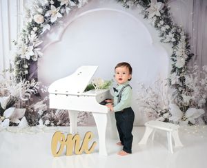 Winter wonderland setup with white piano and floral arch for first birthday shoot.