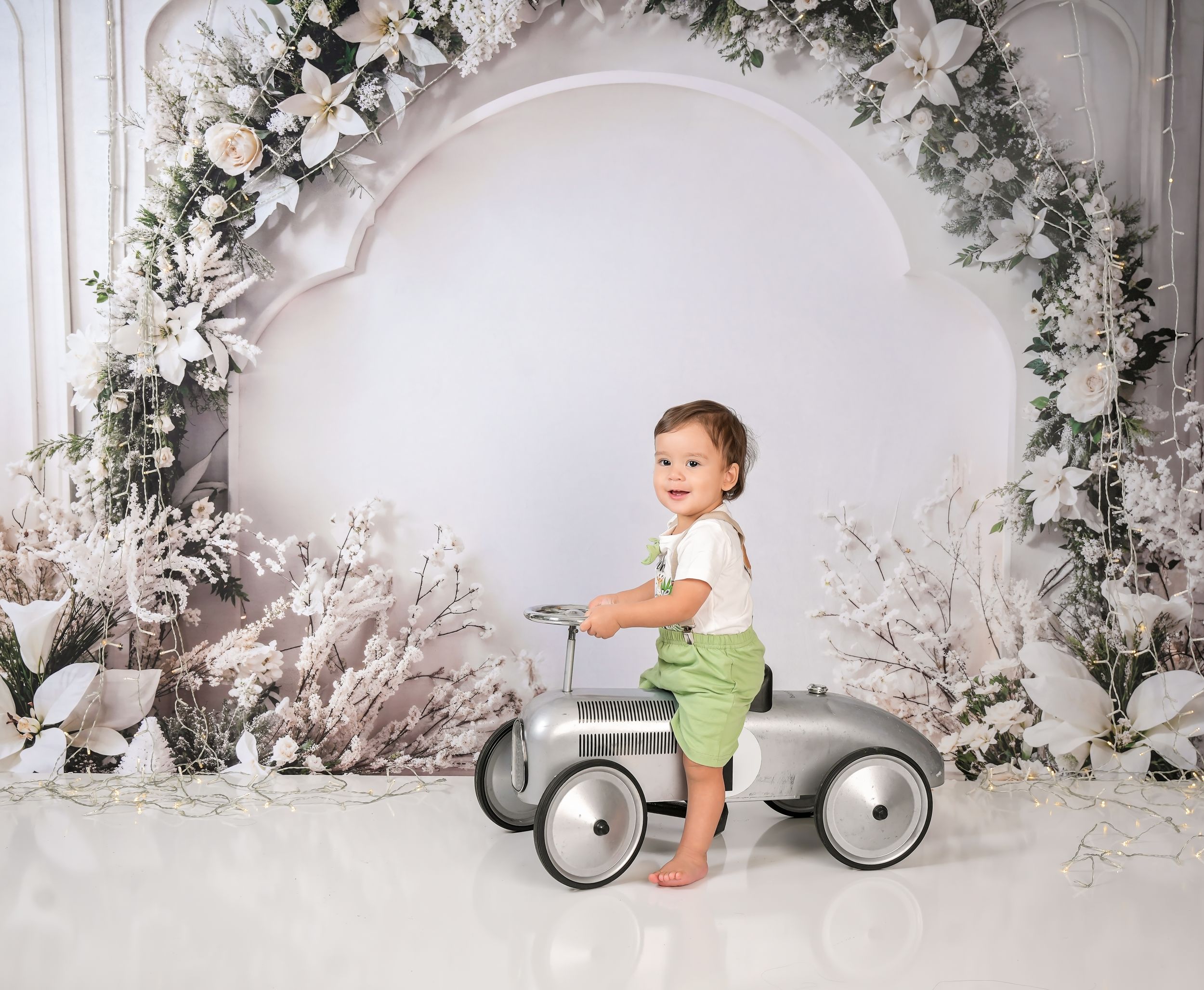 Baby in vintage style riding car prop against white winter wonderland backdrop.