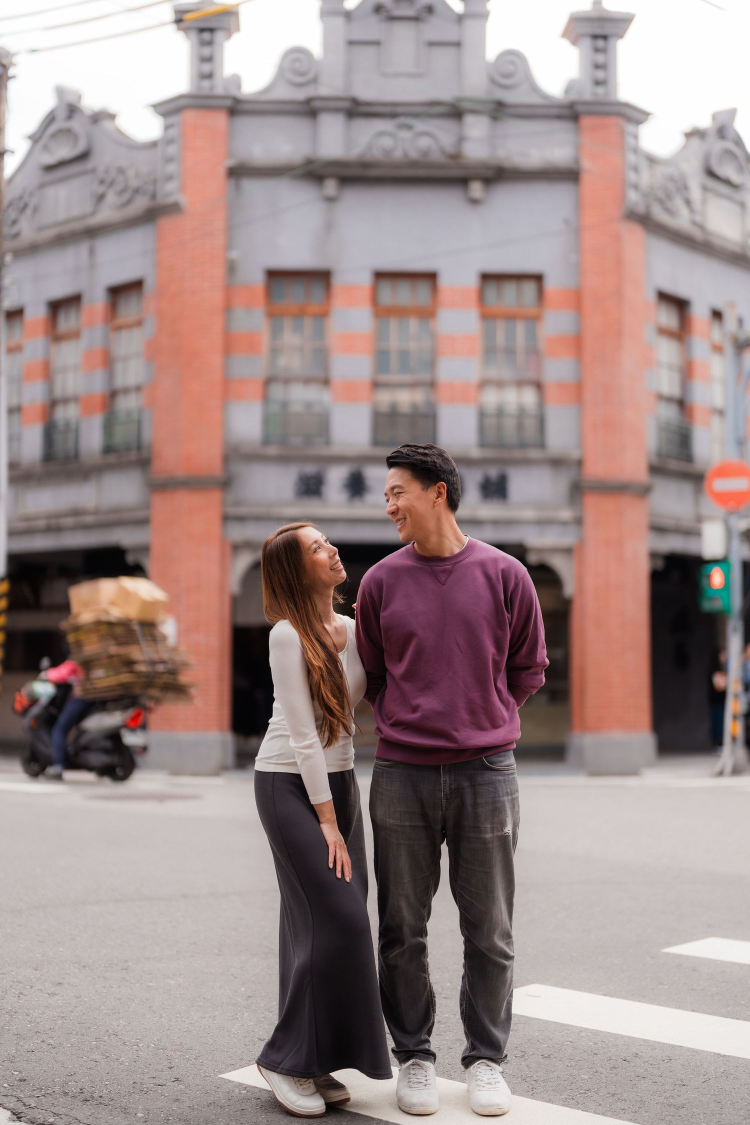 A couple shares a playful moment in front of a historic orange and grey building at Dihua Street in Taipei.
