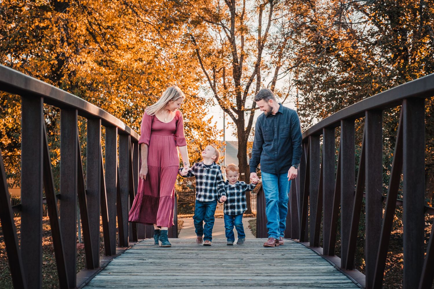 Family portrait captured in autumn setting with tall trees and fallen leaves.