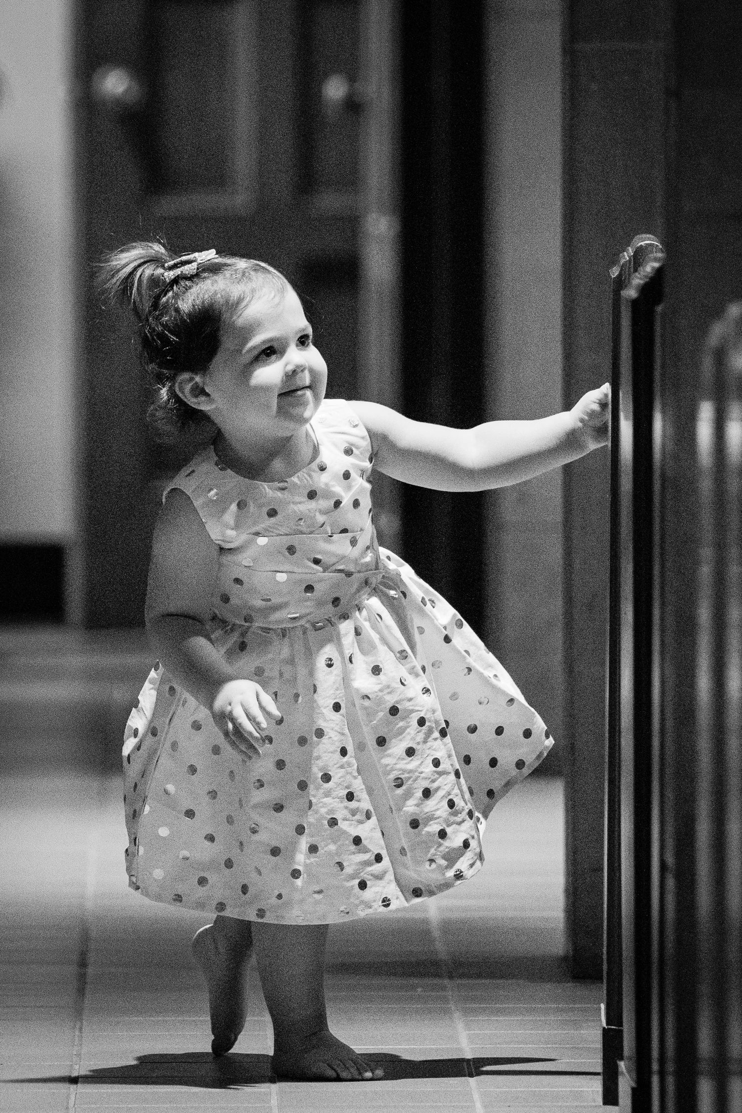 A joyful young child in a polka dot dress twirls and dances in black and white.