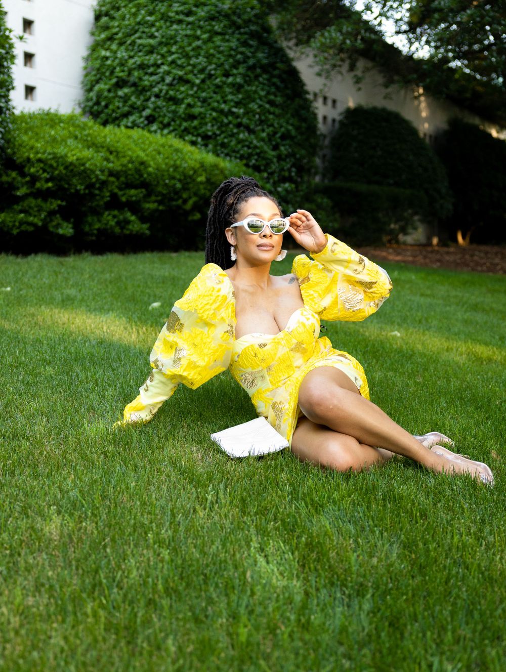 A bright yellow floral dress contrasts with lush green grass in an outdoor summer fashion photography scene.