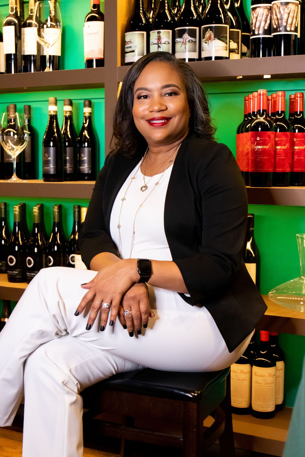 Professional portrait in front of wine bottles and shelves with liquor at a bar or restaurant with green lighting in background.