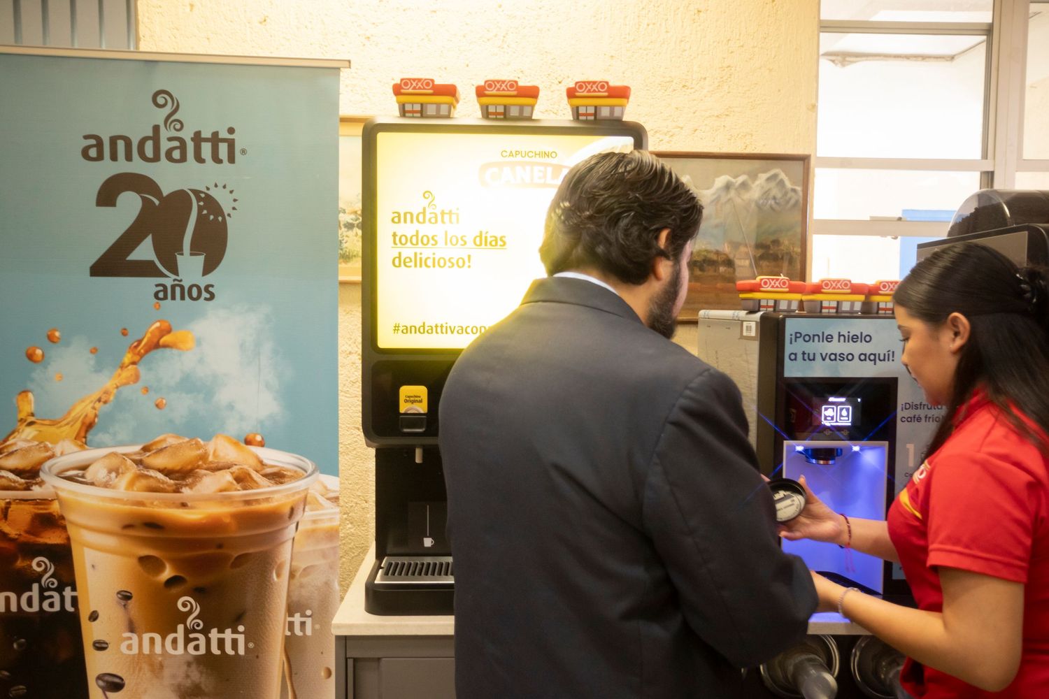 Customer ordering at a coffee shop counter with beverage machines and an Andatti 20 years promotional display visible.