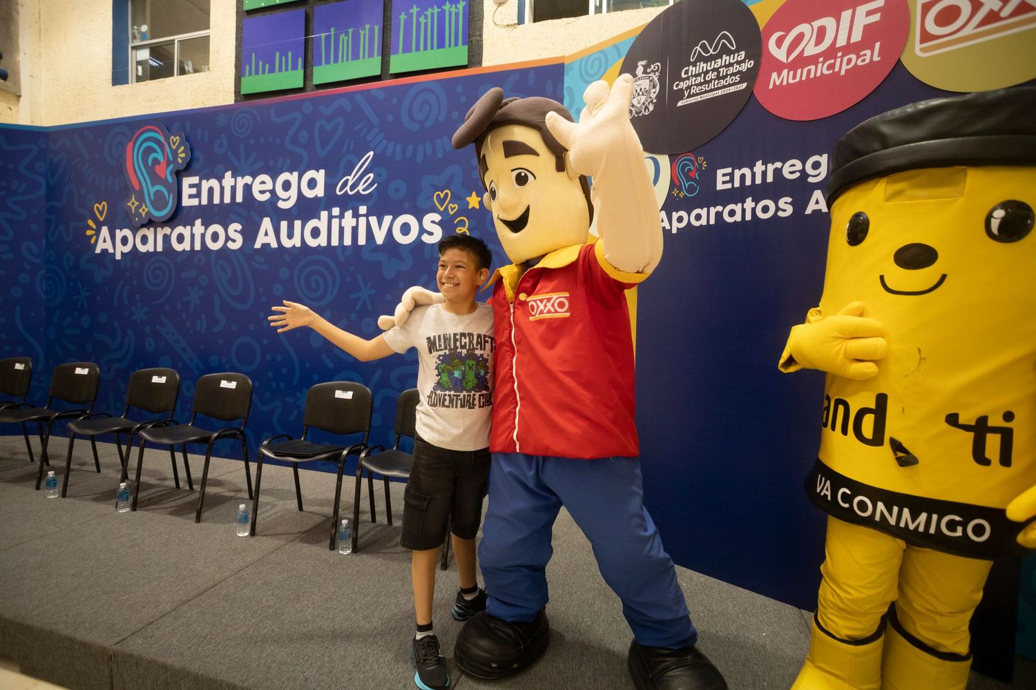 A series of colorful mascot characters and performers interacting at an indoor event with blue wall backgrounds.