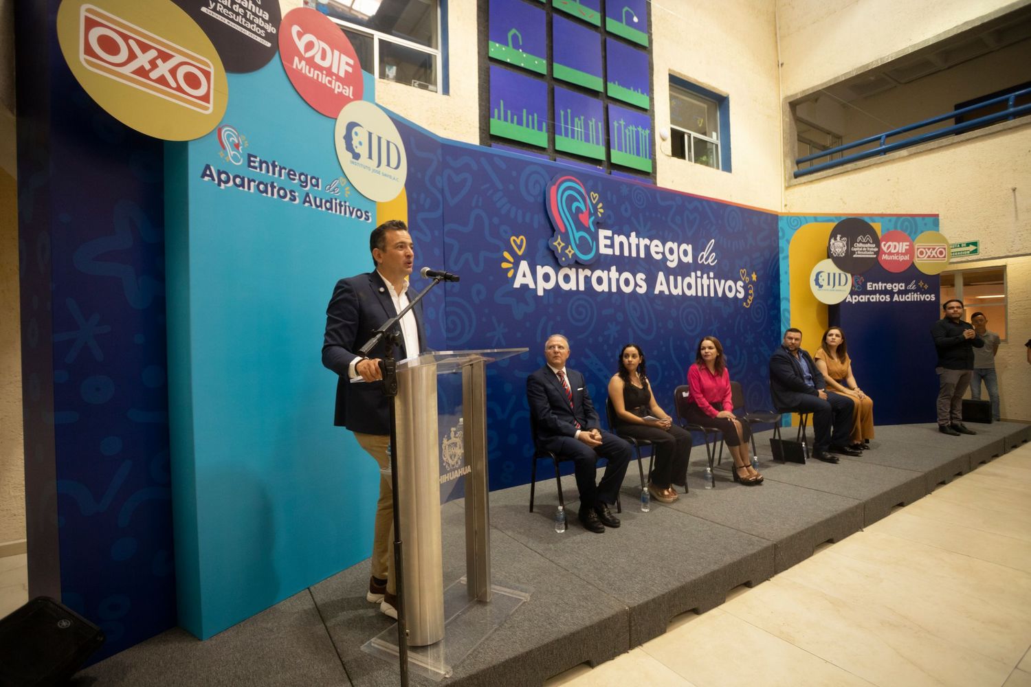 A person sits in a blue-walled office hallway with corporate signage and chairs along the wall.