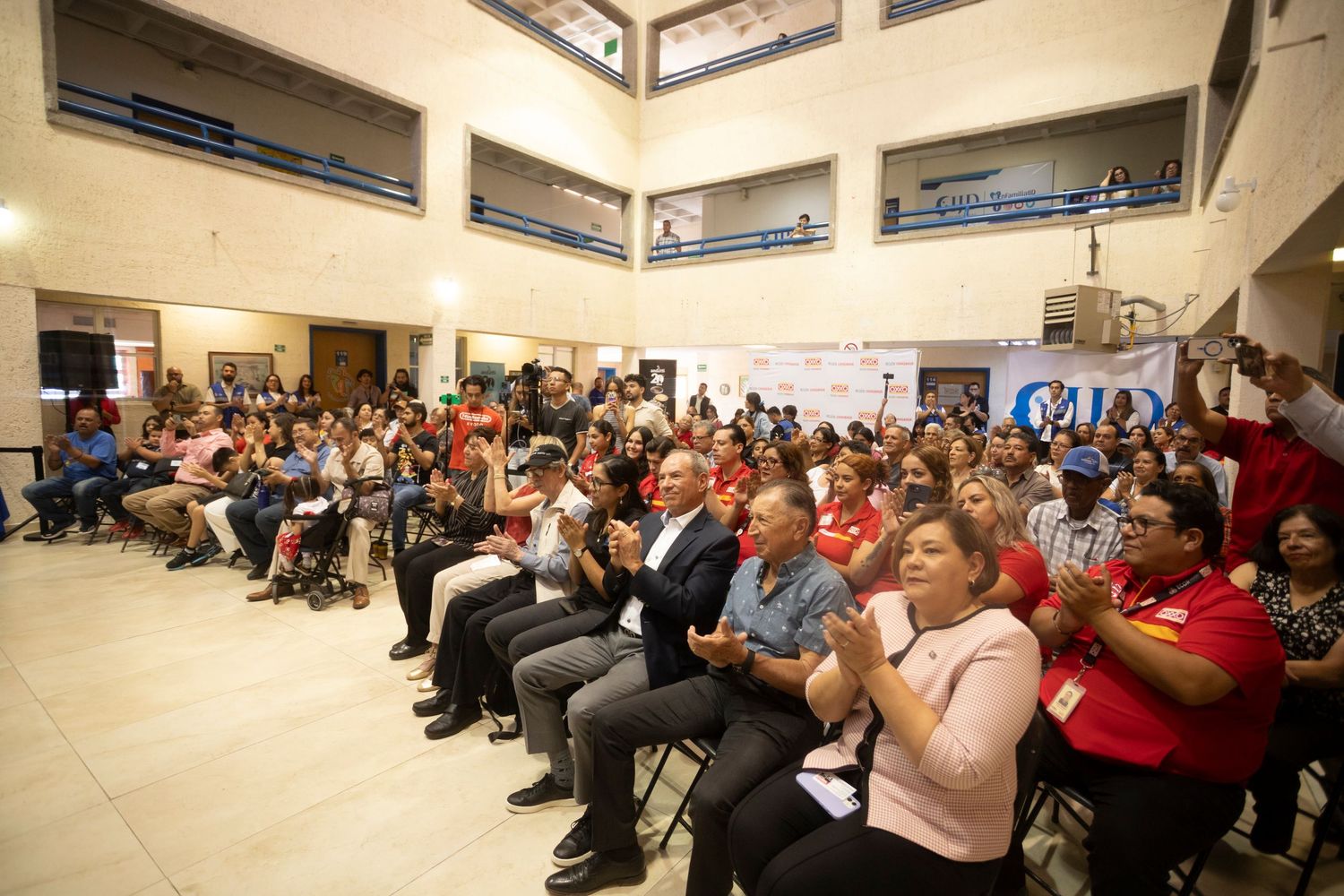 Large audience seated in rows at a conference or presentation venue with bright overhead lighting.