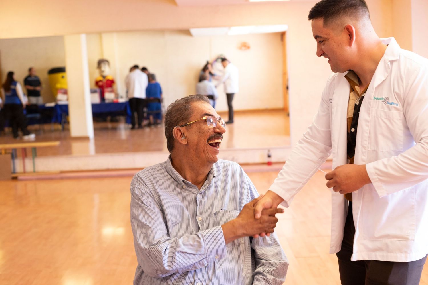 A medical professional in a white coat interacts with a smiling patient in a healthcare facility hallway.
