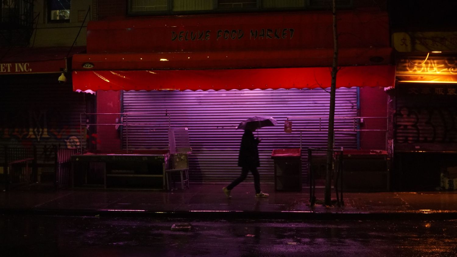 Silhouette of person walking past storefront with red neon lighting in the rain.