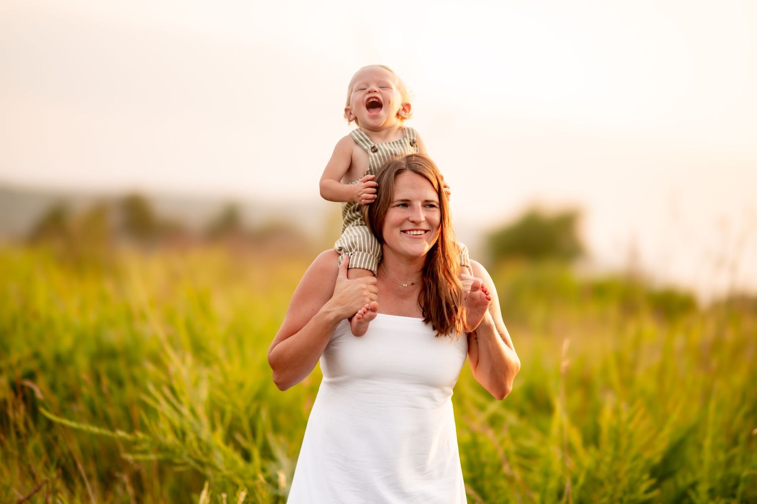 A joyful moment shared in a sunny meadow as a parent gives a shoulder ride among tall grass at sunset.