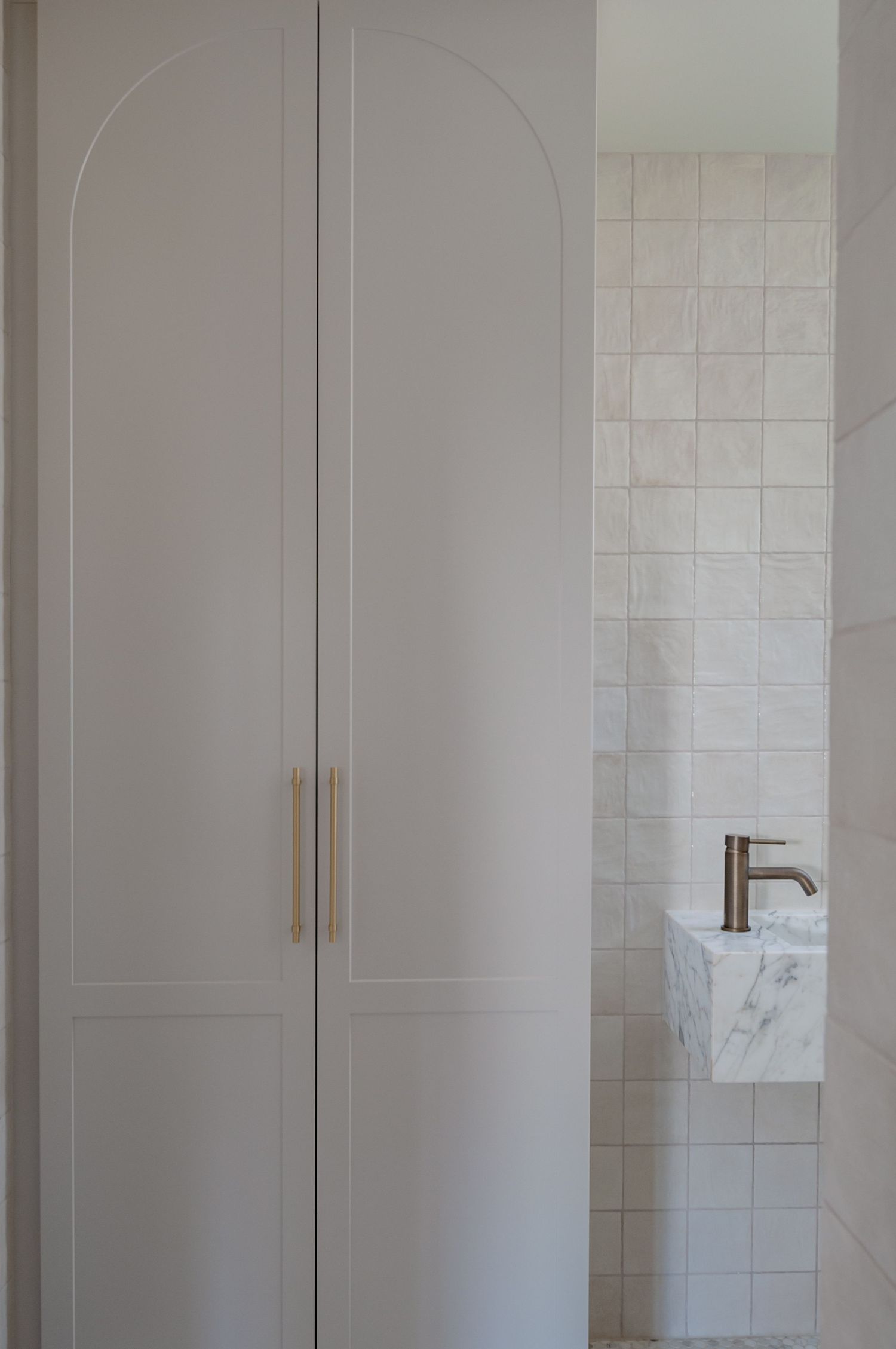 Minimalist bathroom storage featuring white arched cabinet doors and marble accents with modern fixtures.