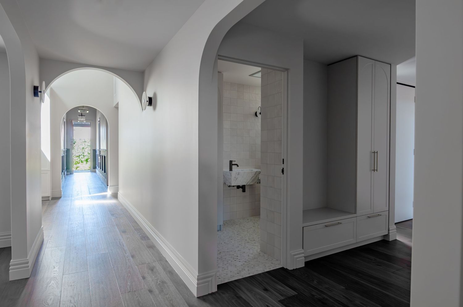 Long white corridor with arched doorways, built-in storage, and hardwood flooring illuminated by natural light.