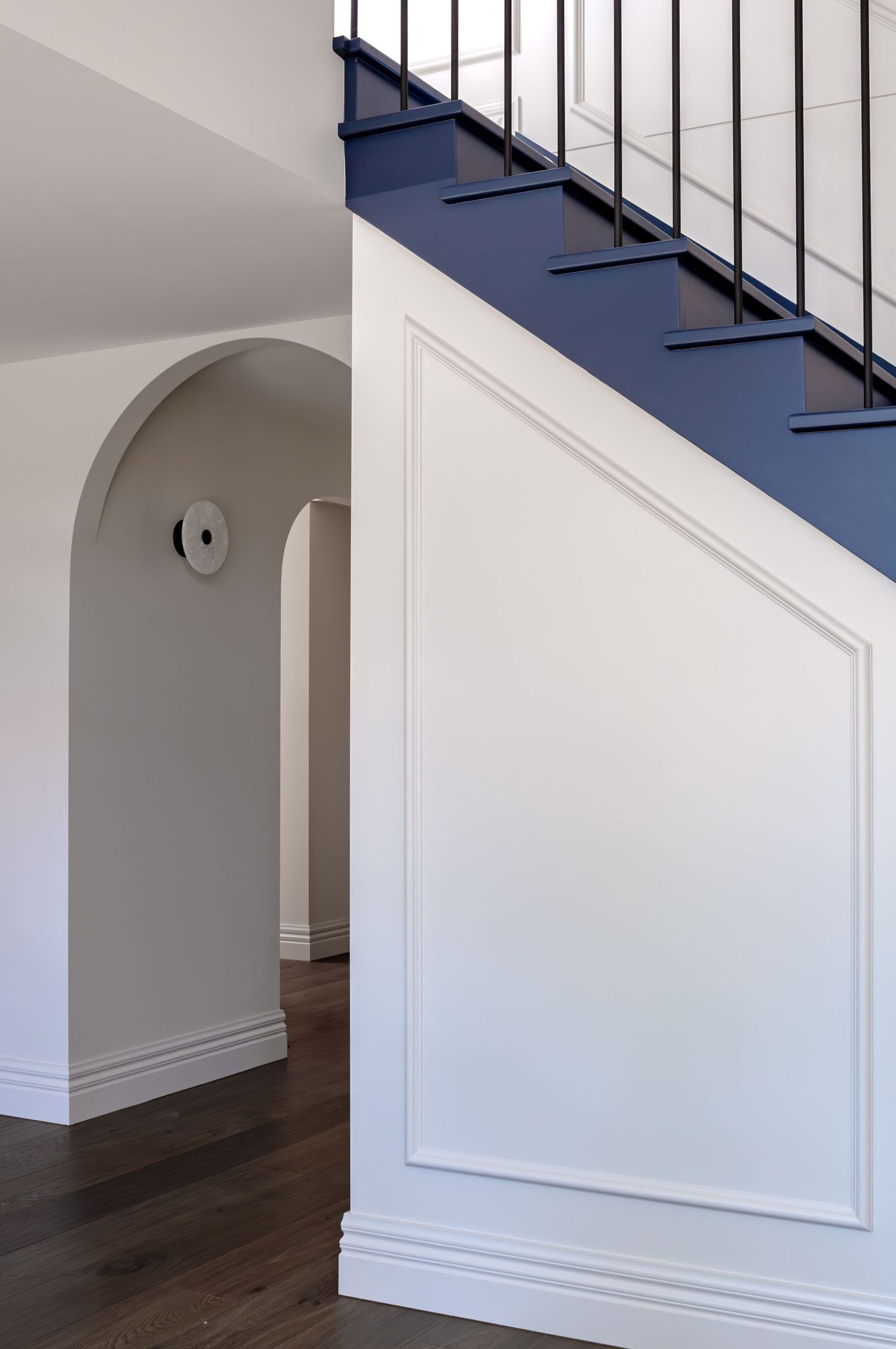 Architectural detail of white staircase with navy blue treads and black metal railings beside an arched doorway.