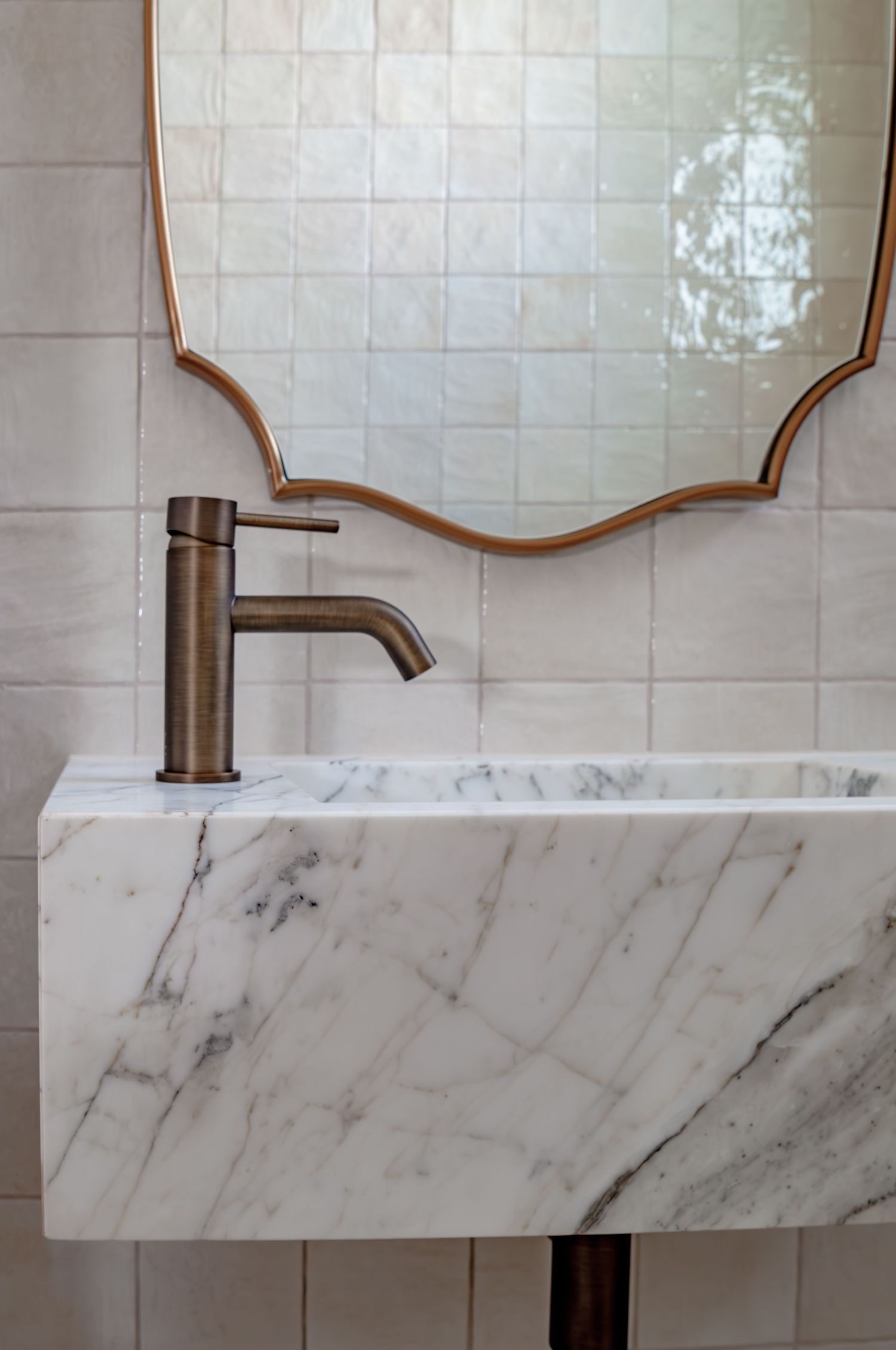 Elegant bathroom vanity featuring marble floating sink, bronze faucet, and decorative mirror against white tile.