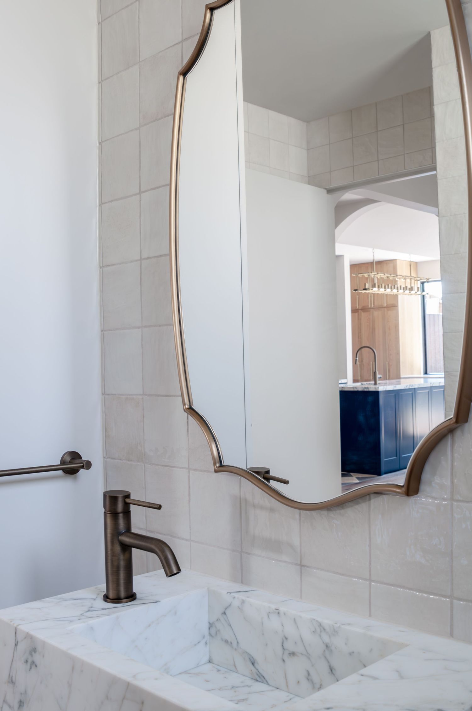 Modern bathroom vanity featuring a marble countertop sink and curved bronze-framed mirror against white tiled walls.