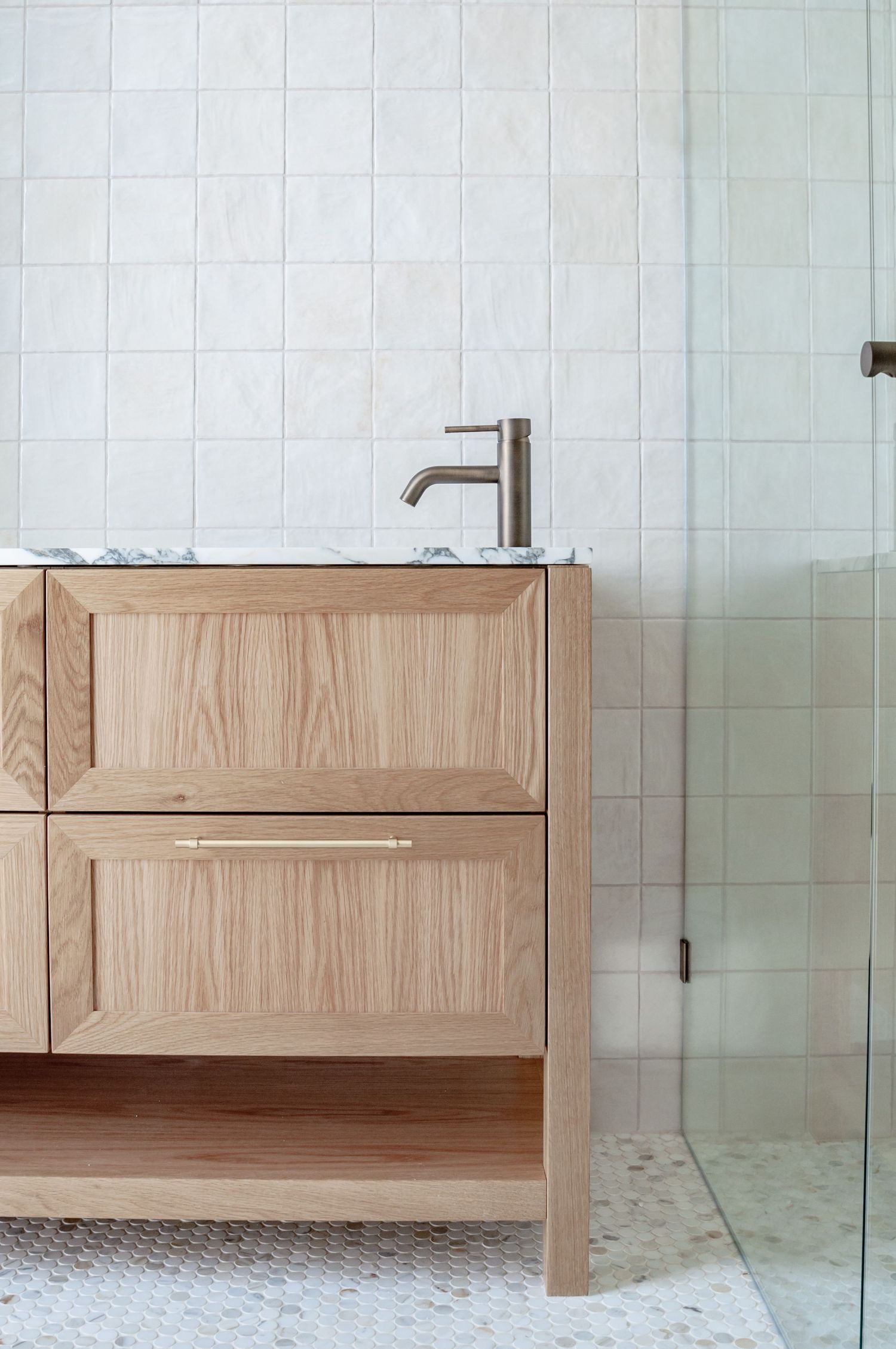 Light wood bathroom vanity with brushed nickel faucet against white square tiled wall.