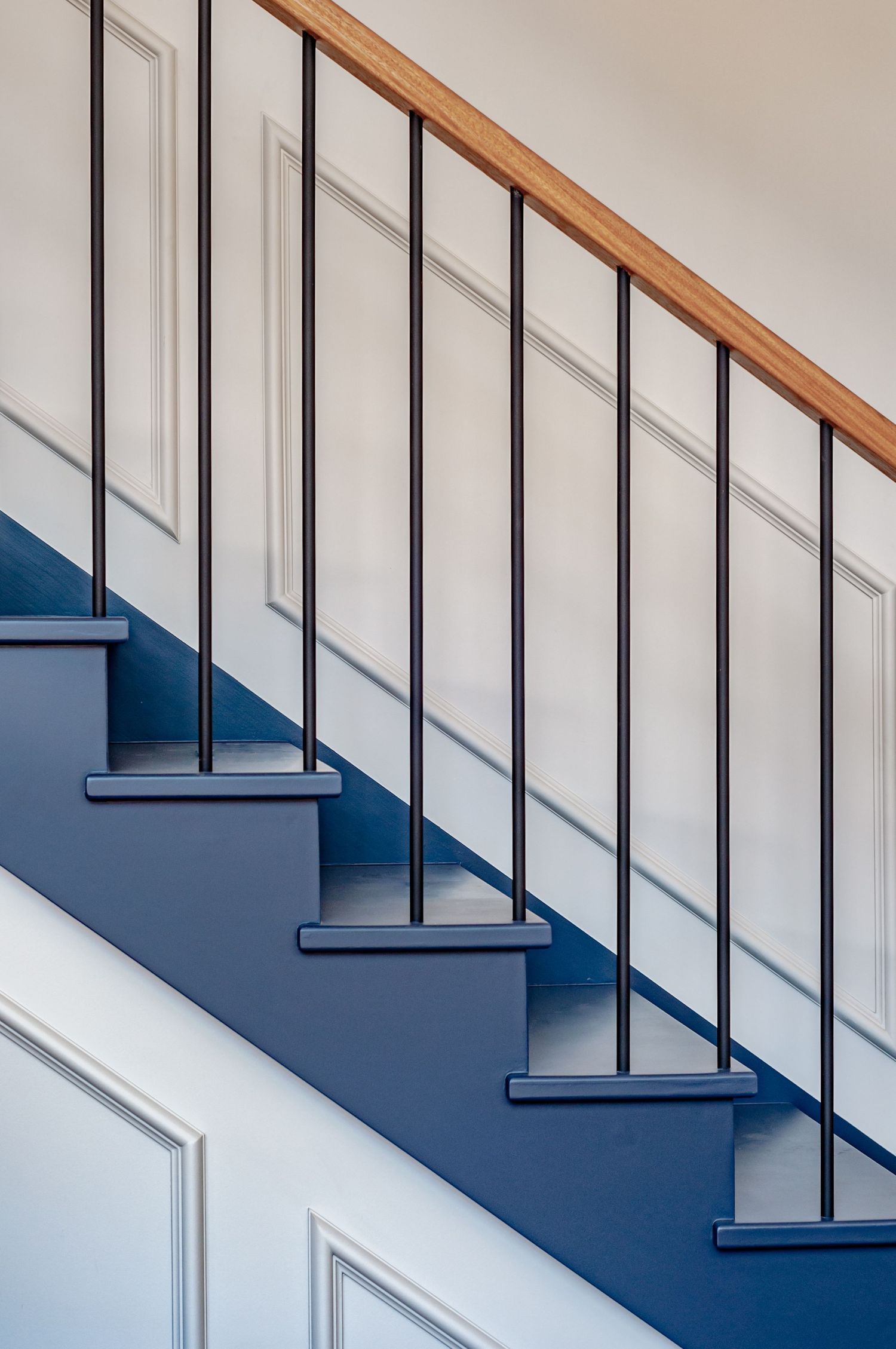 Modern staircase with navy blue steps, black metal railings, and wooden handrail against white walls.