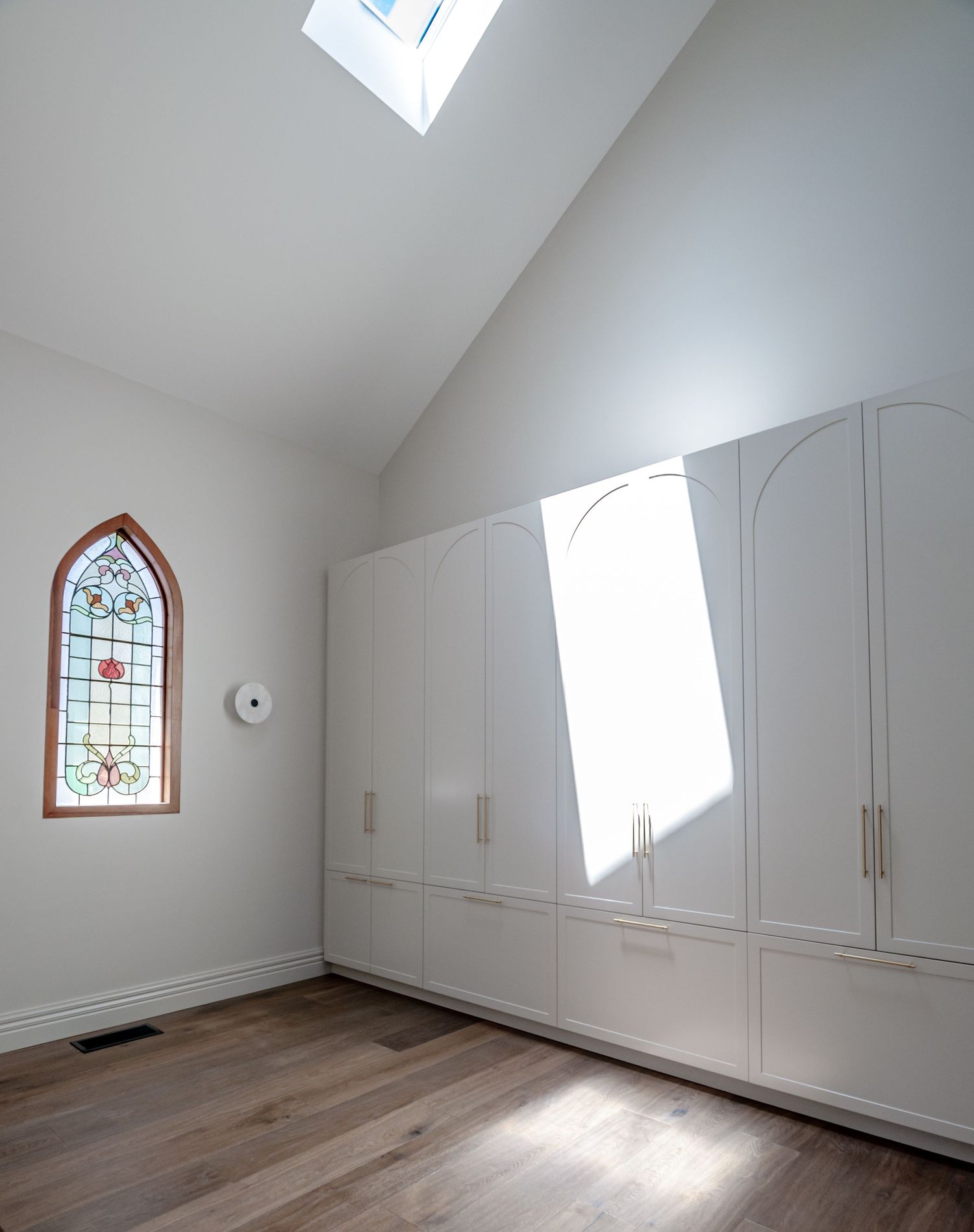 Bright room with built-in white cabinets, hardwood floors, and gothic-style stained glass window.