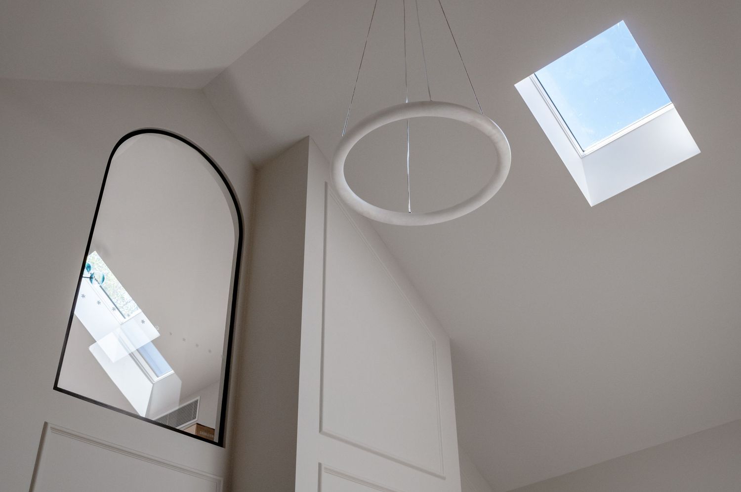 High ceiling interior with arched mirror, circular pendant light, and skylight window.