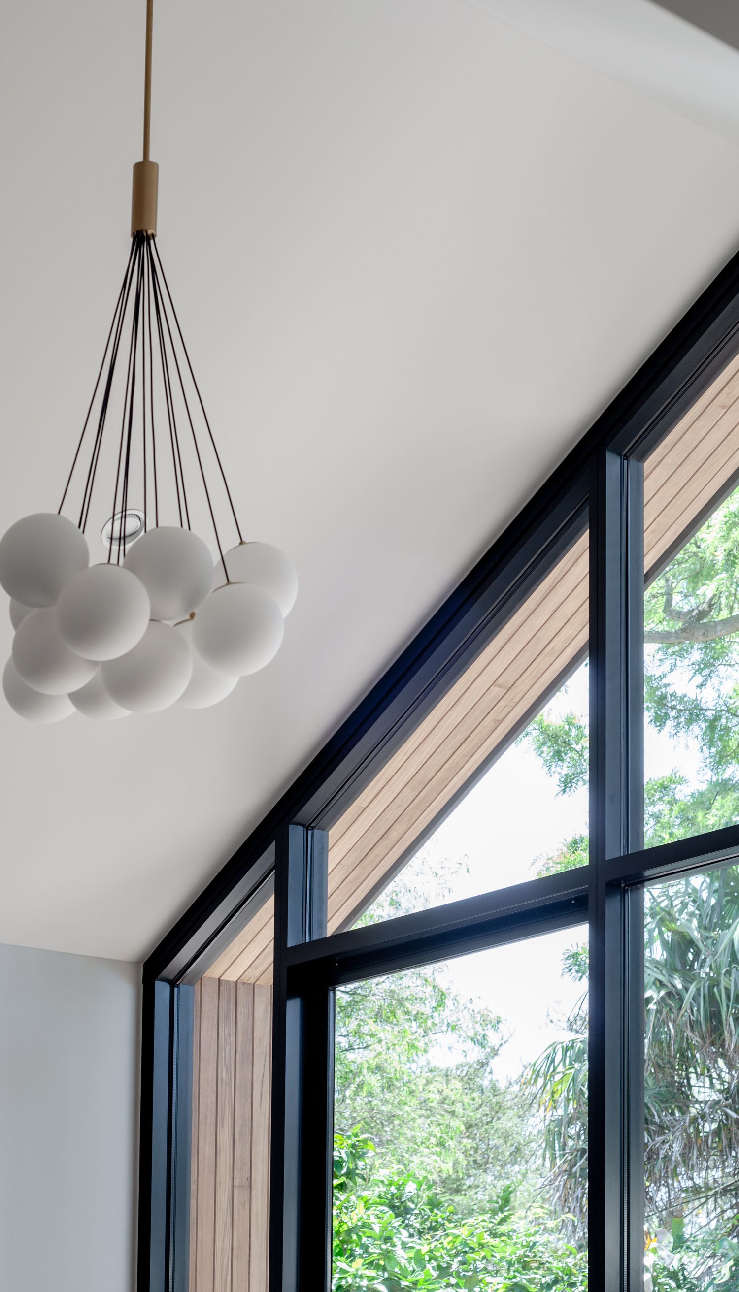 Modern cluster pendant light with white globe bulbs hanging near large angled window.
