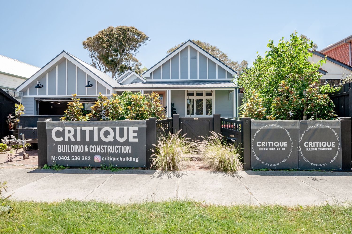 Blue house exterior with construction company signage and landscaping behind temporary fencing.